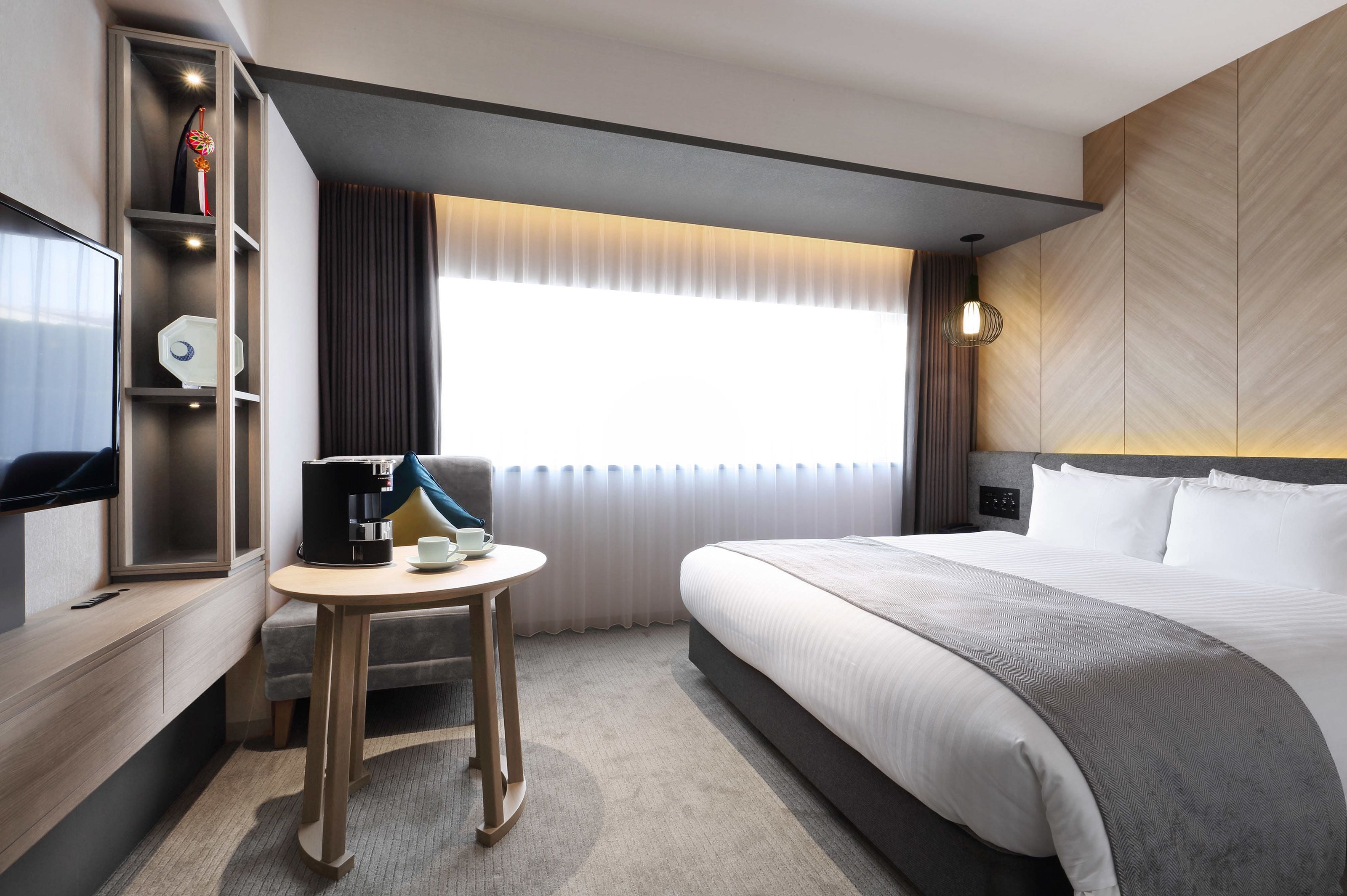 Une chambre d’hôtel avec un lit, un bureau doté d’une machine à café, une télévision et une fenêtre avec des rideaux.