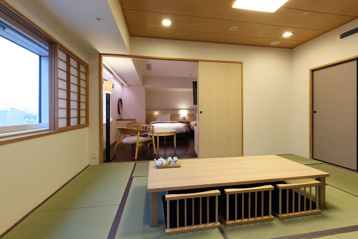 A traditional Japanese-style room with tatami flooring, a low wooden table with benches, and a sliding door leading to a bedroom.