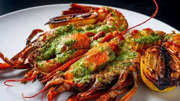 A plate of grilled lobster with a green sauce and grilled lemon slices.