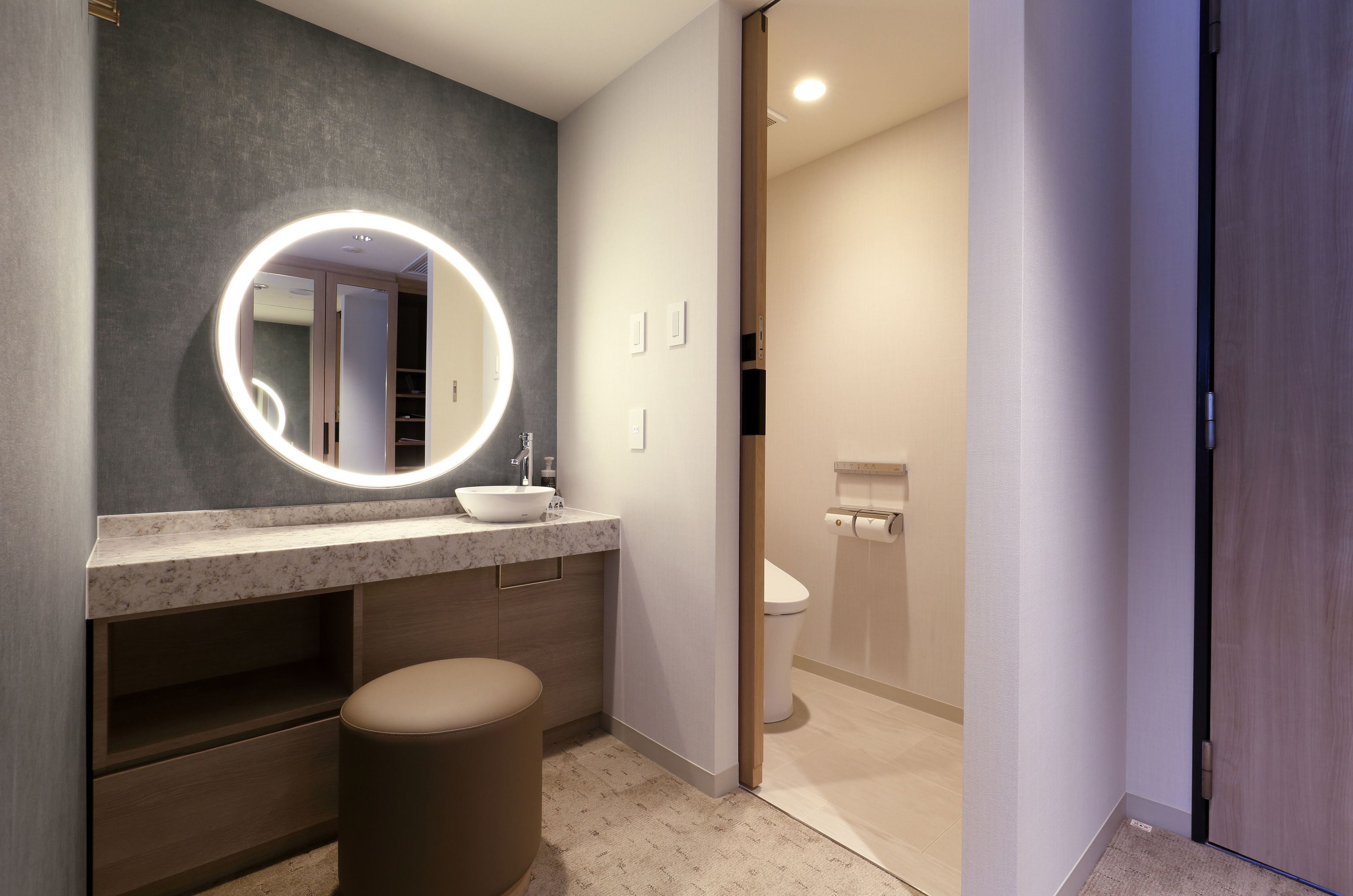 A modern bathroom with a round mirror, a sink, and a toilet.