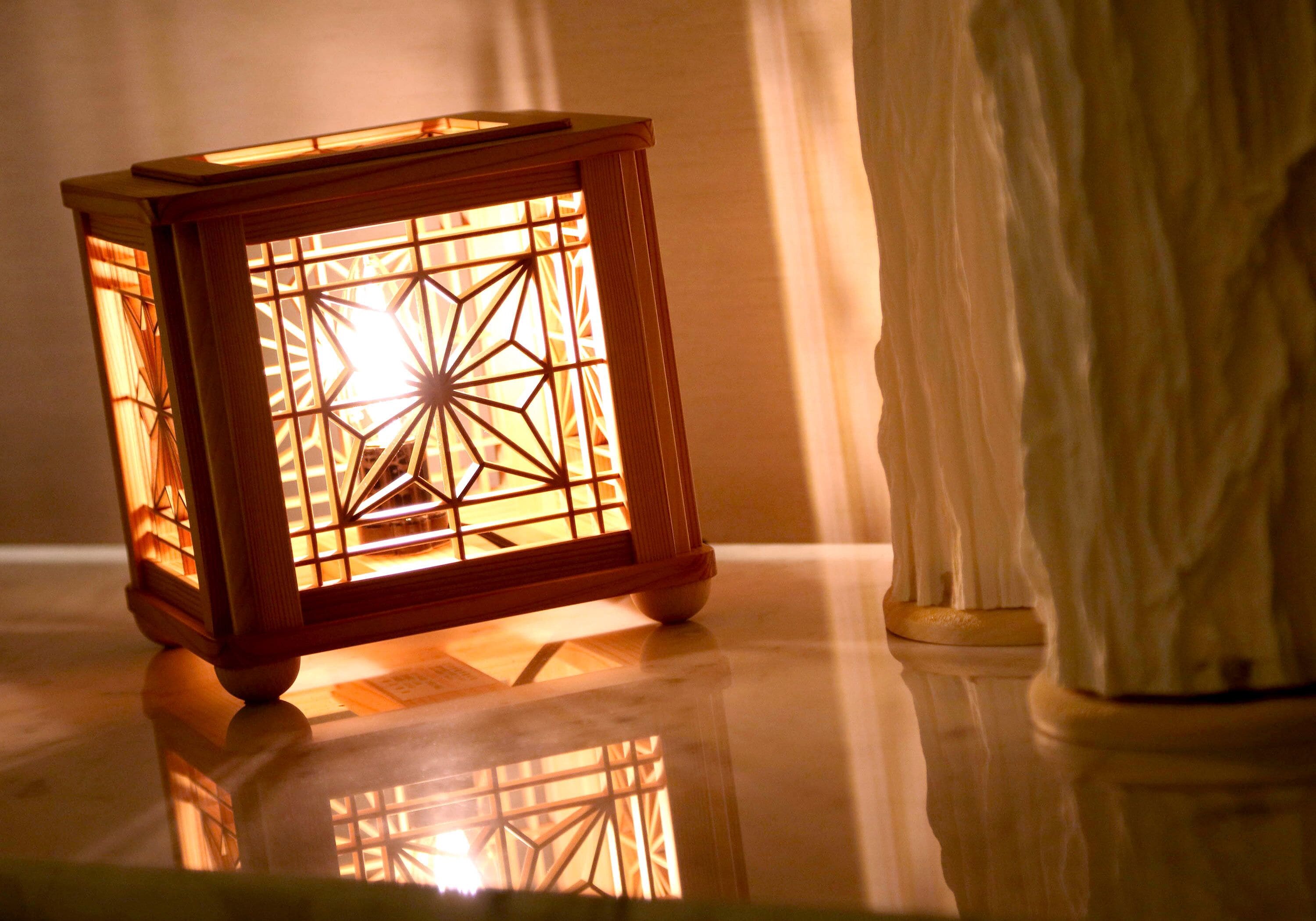 A wooden lantern with a geometric pattern, placed on a reflective surface next to a white statue.