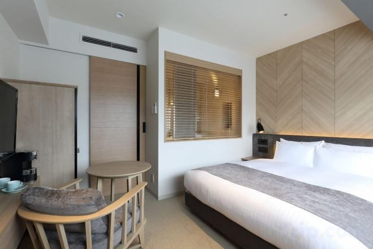 A hotel room with a bed, a desk, a chair, and a window with blinds.