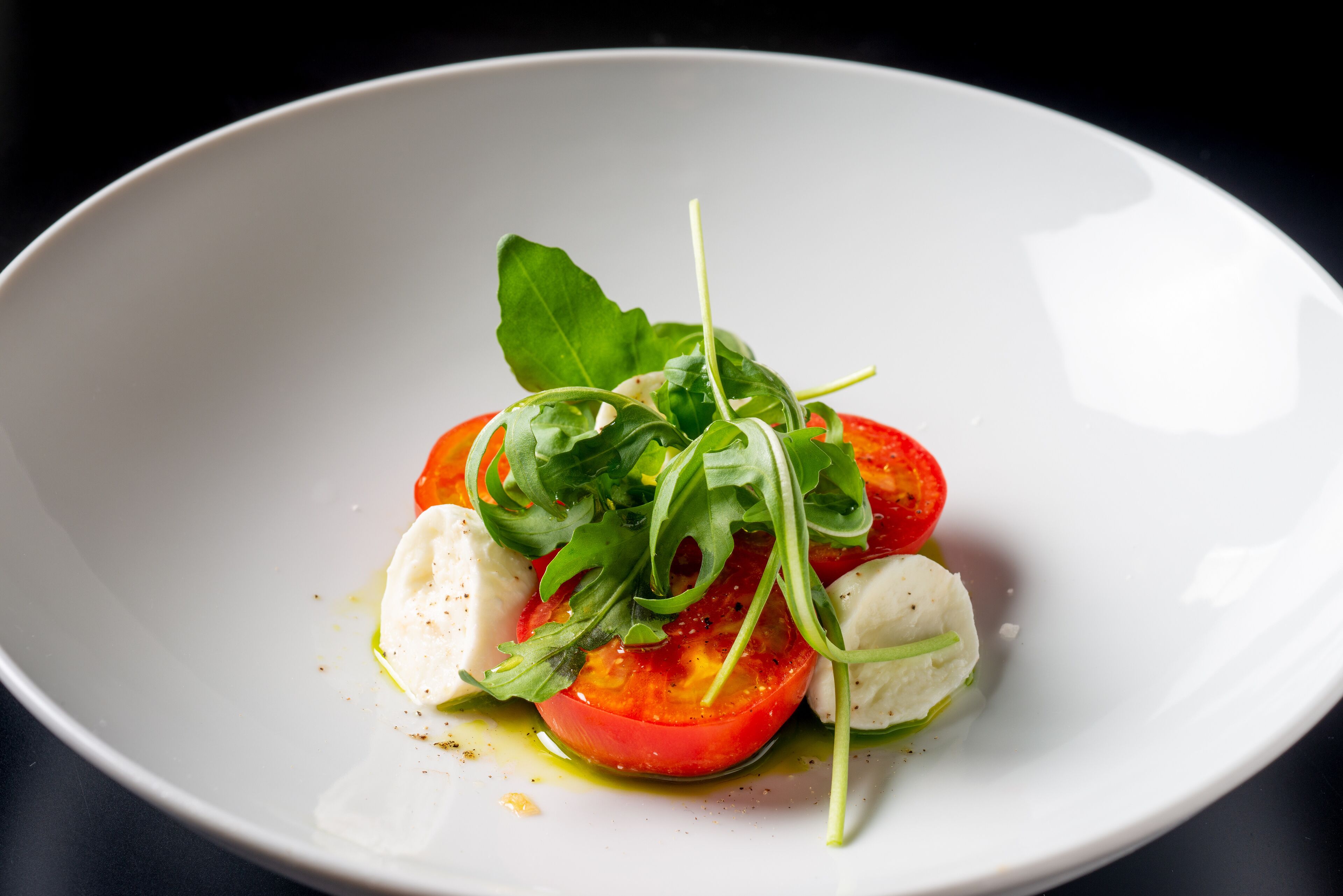 A white plate with a salad consisting of tomatoes, mozzarella, and greens.