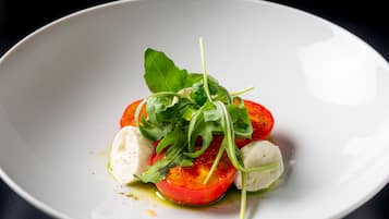 A white plate with a salad consisting of tomatoes, mozzarella, and greens.