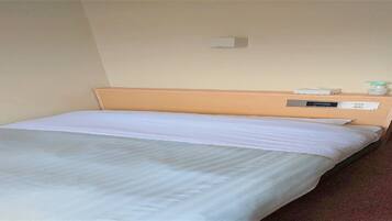 Een enkel bed met een houten hoofdbord, een witte matras en een klein nachtkastje met een lamp en een stopcontact.