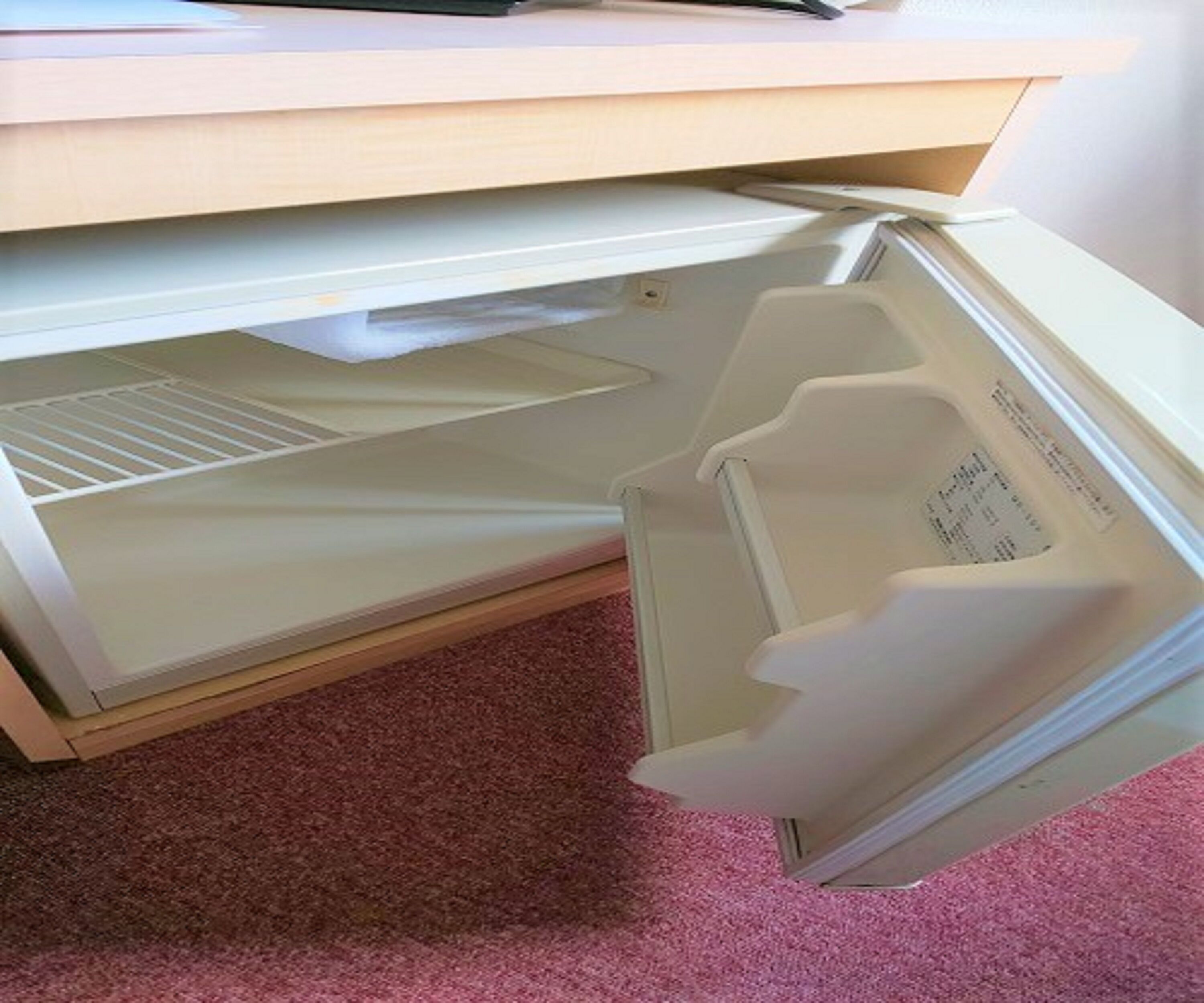 A drawer under a desk with a pink carpet.