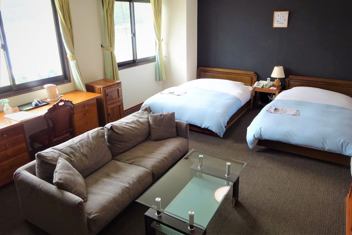 Una habitación de hotel con dos camas, un sofá, un escritorio y una mesa de centro de vidrio.