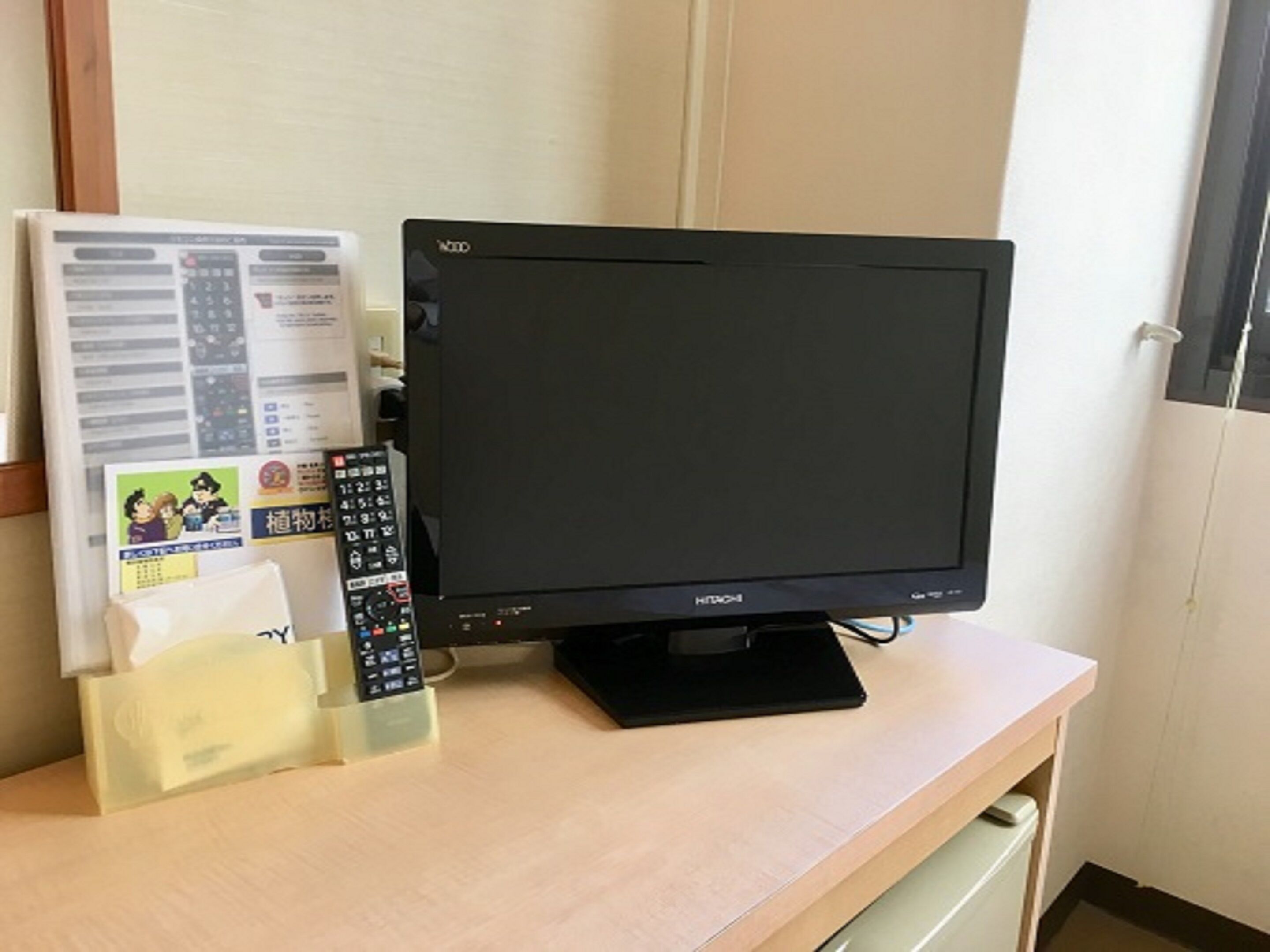 A television on a wooden desk with a remote control and a paper with text and images.