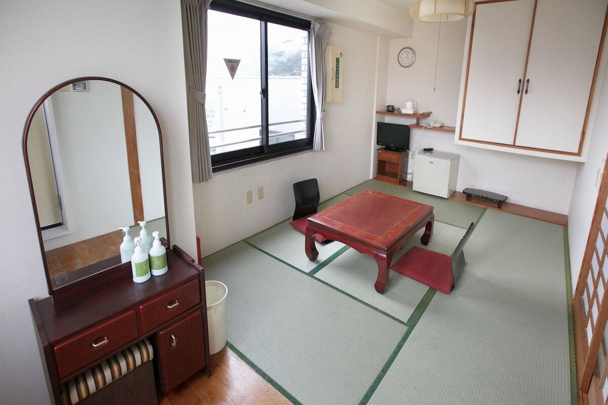 Una habitación tradicional japonesa con suelo de tatami, una mesa de madera, un mueble bajo con artículos de aseo, un espejo y un armario.