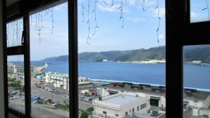 A view from a window overlooking a coastal city with buildings and a body of water. - Amami Port Tower Hotel (Amami)