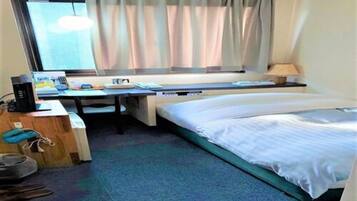 Una habitación de hotel con cama, escritorio, computadora y ventana con cortinas.