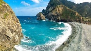 A coastal landscape with rocky cliffs, clear turquoise waters, and a pebbly beach. - Amami Port Tower Hotel (Amami)
