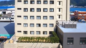 A multi-story hotel with a flat facade, numerous windows, and a parking area in front. - Amami Port Tower Hotel (Amami)