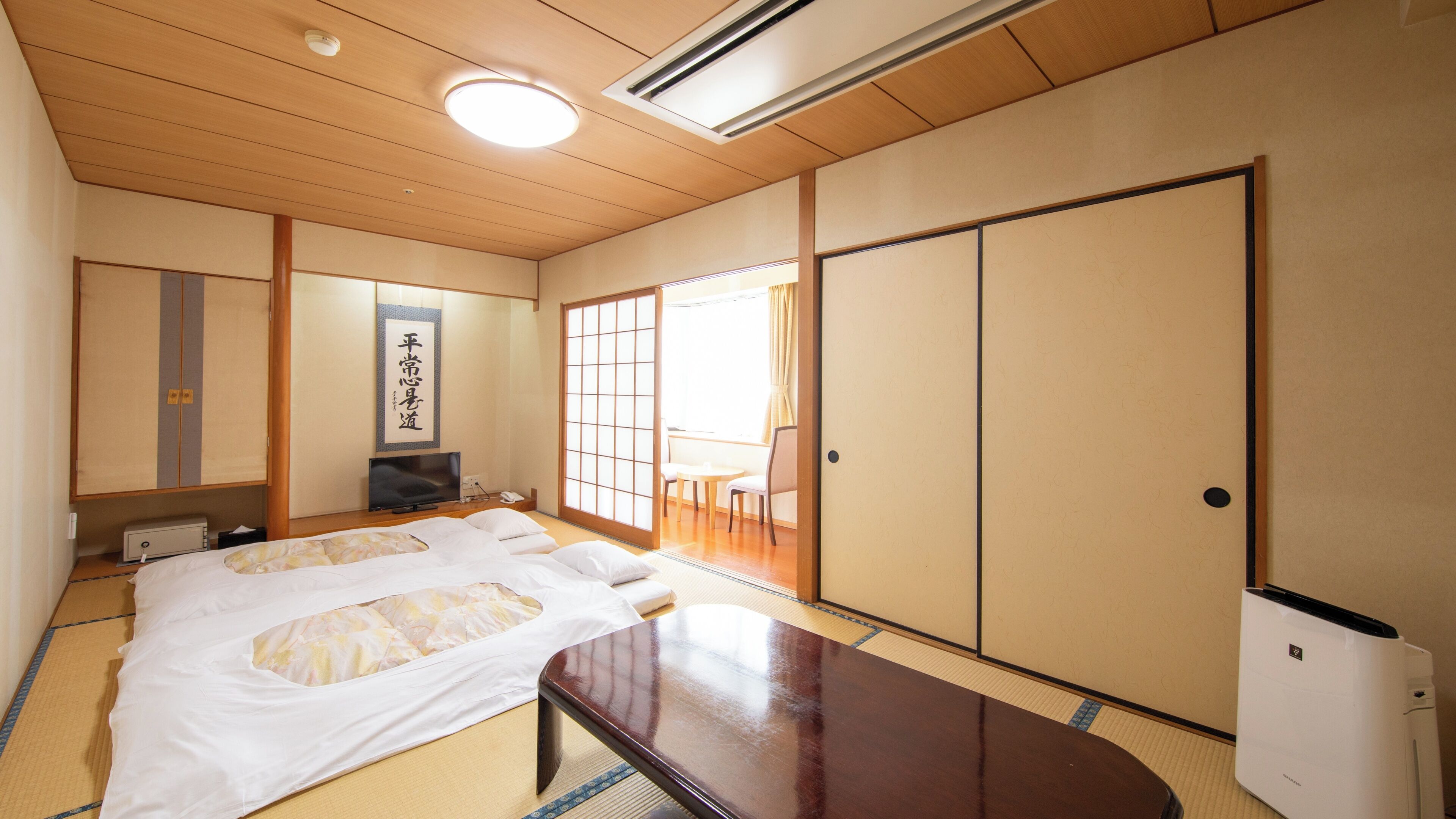 A traditional Japanese room with tatami flooring, a bed with white bedding, a television, a sliding door, and a ceiling fan.