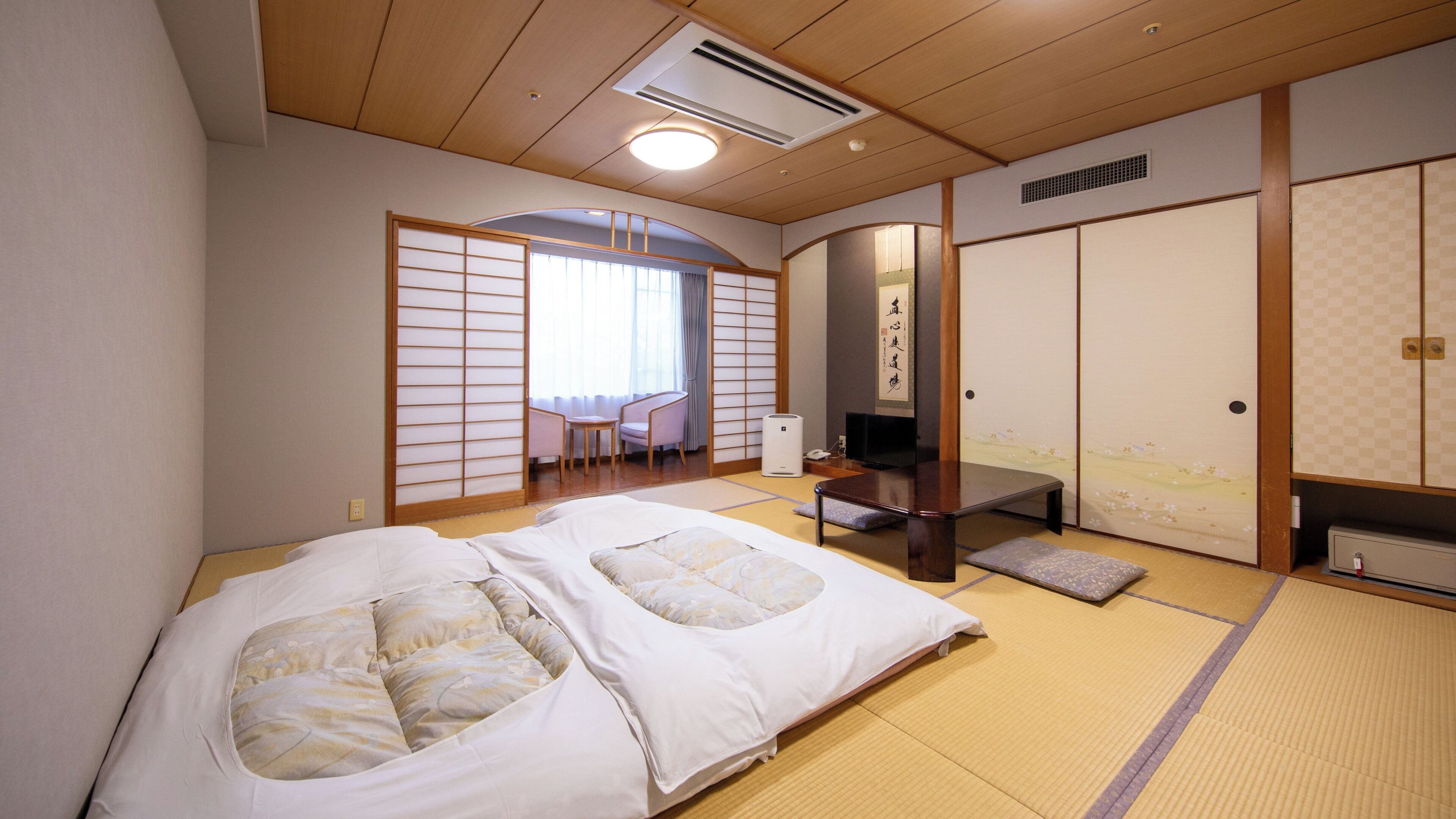 A traditional Japanese-style room with tatami flooring, a futon bed, a desk, and a sliding door.