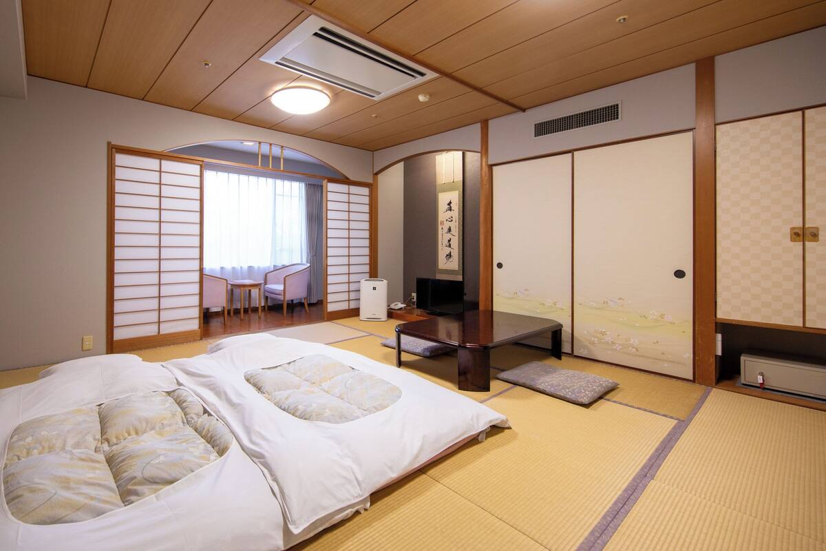 A traditional Japanese-style room with tatami flooring, a futon bed, a desk, and a sliding door.