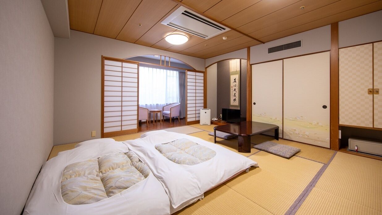 Ein traditioneller japanischer Raum mit Tatami-Böden, einem Futonbett, einem niedrigen Tisch und Schiebetüren.