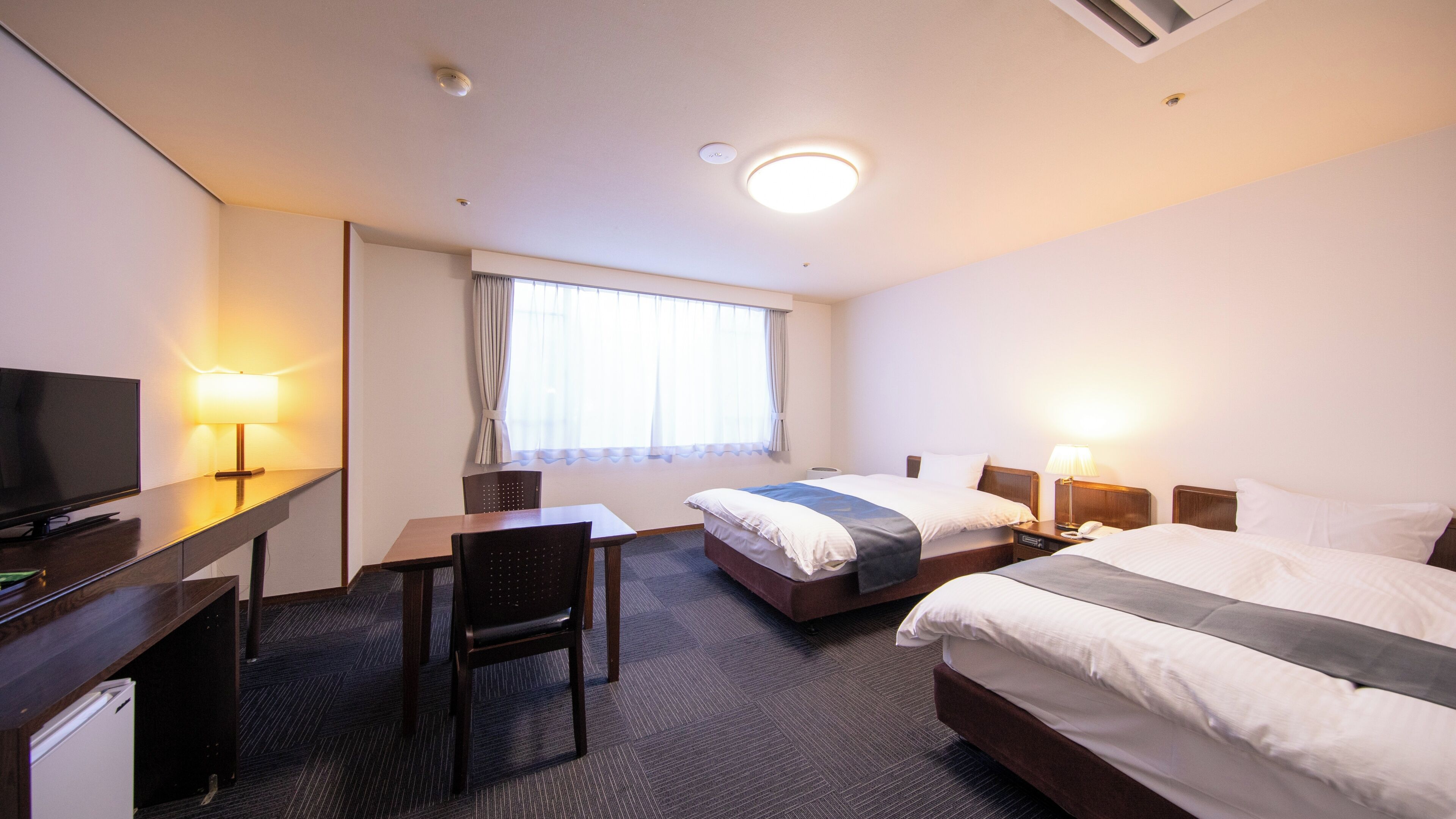 A hotel room with a bed, a desk, a chair, a television, and a window with curtains.