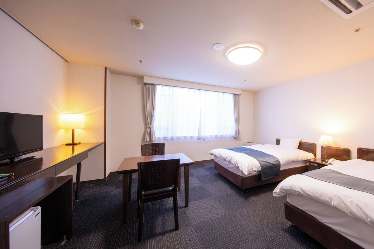 A hotel room with a bed, a desk, a chair, a television, and a window with curtains.