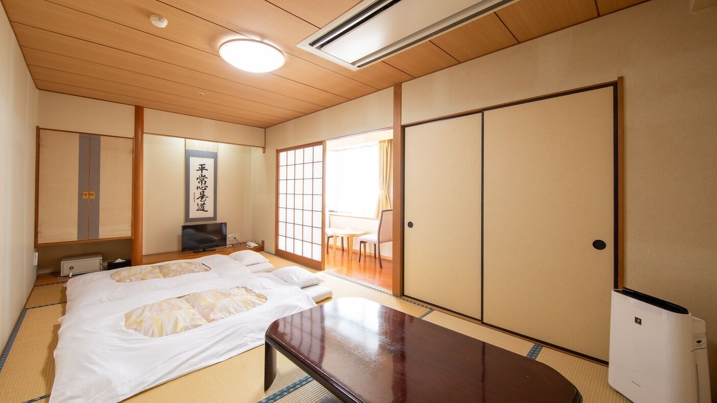 Ein traditioneller japanischer Raum mit Tatami-Böden, einem Futonbett, Schiebetüren und einem Fernseher.