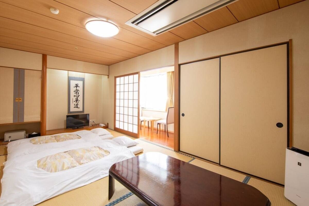A traditional Japanese room with tatami flooring, a futon bed, sliding doors, and a television.
