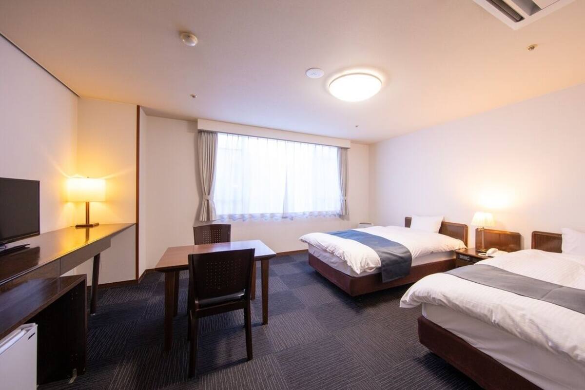A hotel room with two beds, a desk, a chair, a television, and a window with curtains.