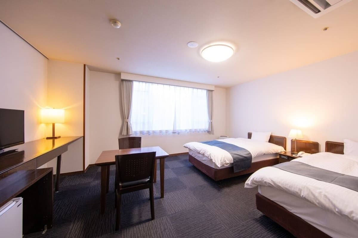 Hotellihuone, jossa on kaksi sänkyä, työpöytä, tuoli, televisio ja ikkuna, jossa on verhot.