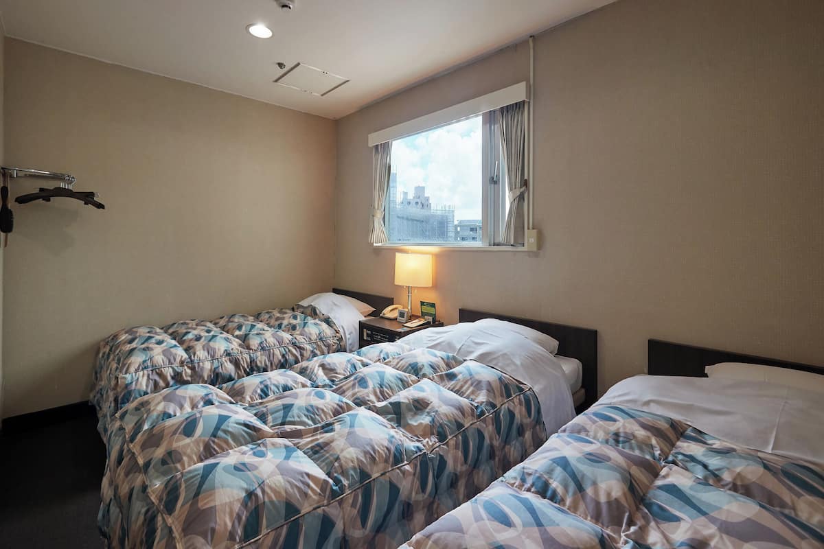 A hotel room with two beds, a window with curtains, a bedside table with a lamp, and a wall-mounted telephone.