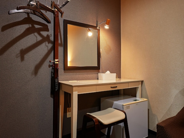 Una habitación de hotel compacta con un escritorio de madera, un espejo, un taburete pequeño y un refrigerador.