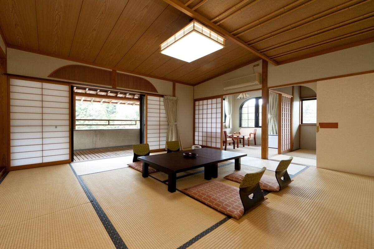 Una habitación tradicional japonesa con suelo de tatami, una mesa baja, sillas y puertas correderas.