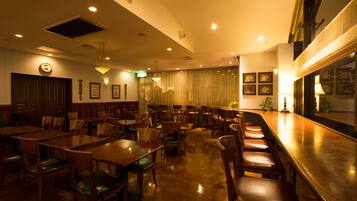 Un restaurante con mesas y sillas de madera, una zona de bar y vistas a la ciudad a través de amplios ventanales.