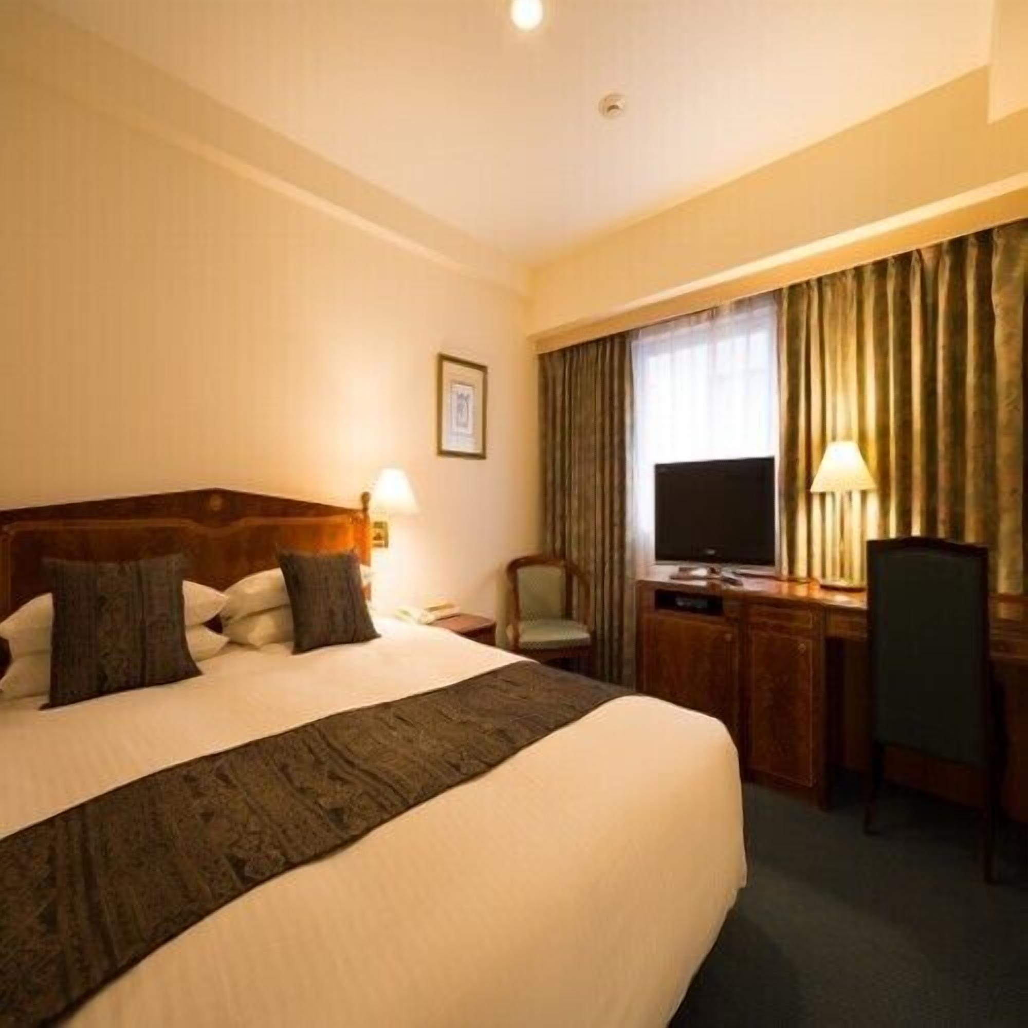 A hotel room with a large bed, a desk with a chair, a television, and a window with curtains.