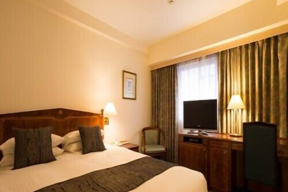 A hotel room with a large bed, a desk with a chair, a television, and a window with curtains.