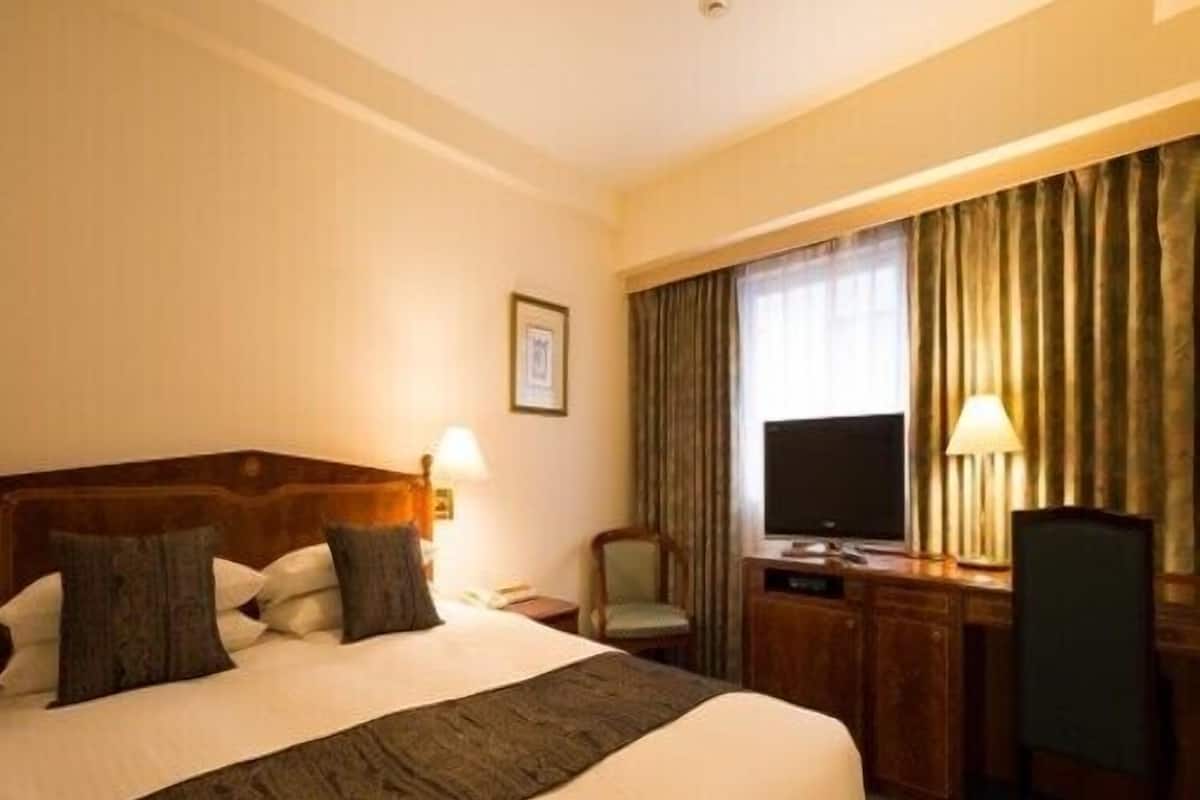 A hotel room with a large bed, a desk with a chair, a television, and a window with curtains.
