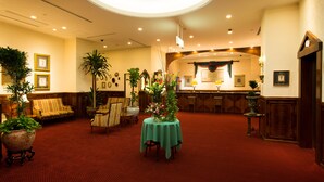 A spacious lobby with a red carpet, a reception desk, and several potted plants.