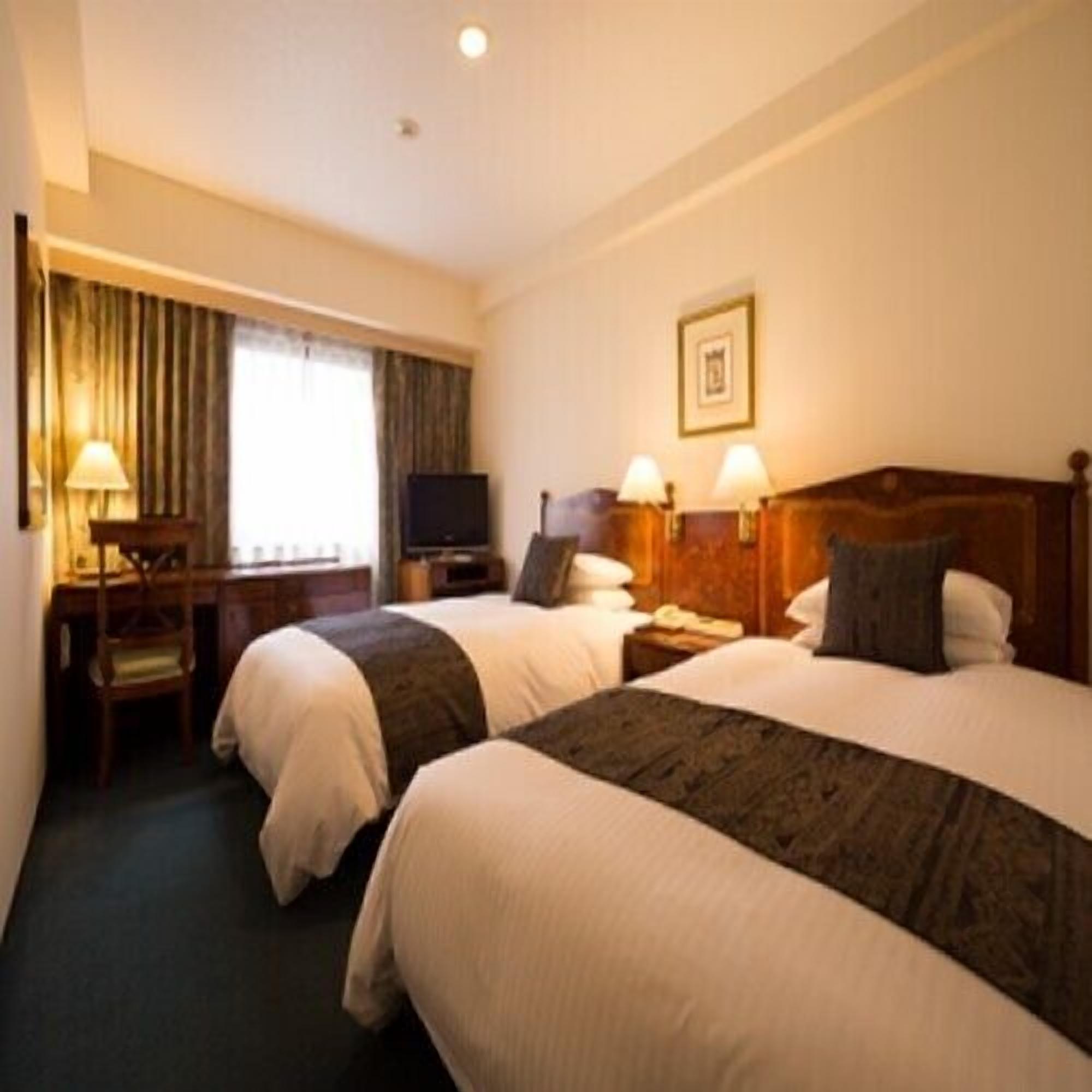 A hotel room with two beds, a desk, a television, and a framed picture on the wall.