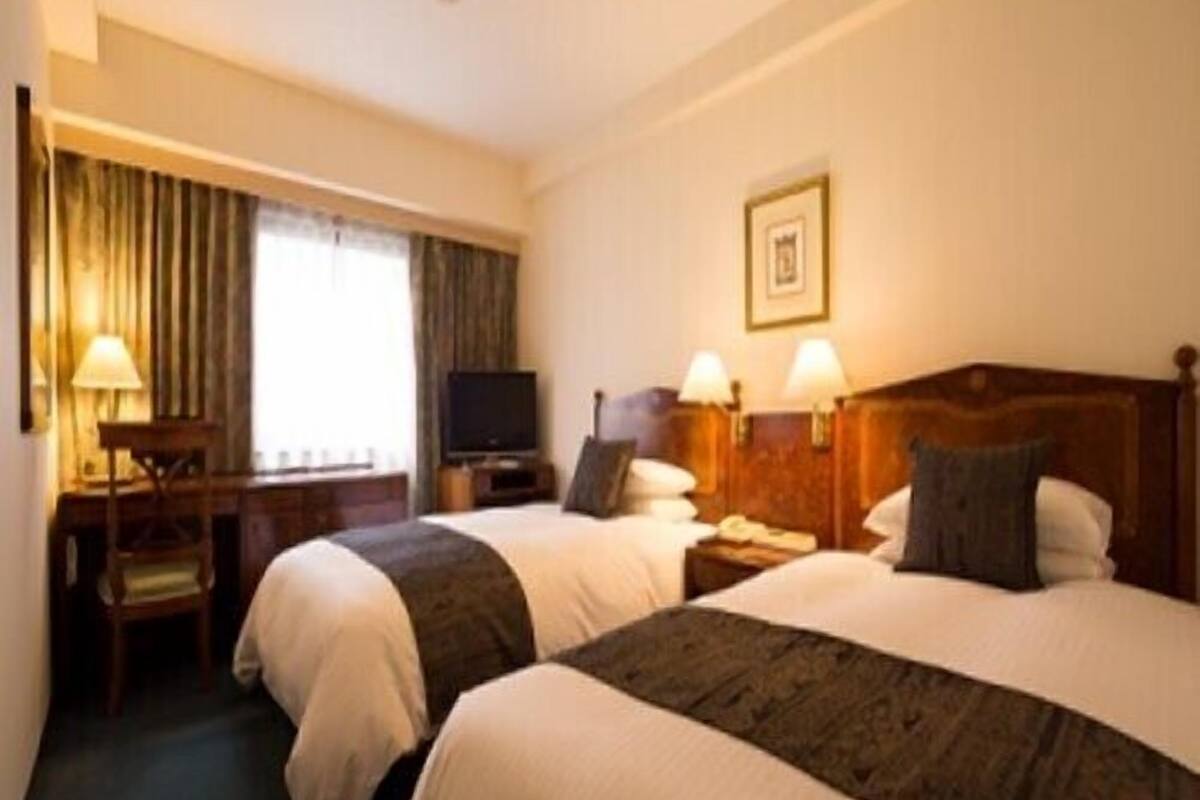 A hotel room with two beds, a desk, a television, and a framed picture on the wall.