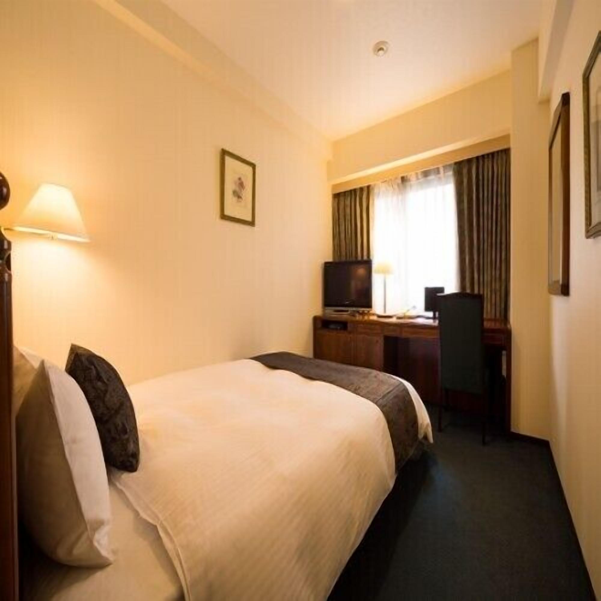 A hotel room with a bed, desk, chair, television, and a picture on the wall.