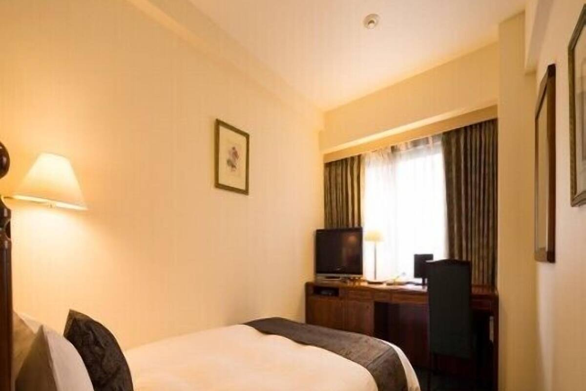 A hotel room with a bed, desk, chair, television, and a picture on the wall.