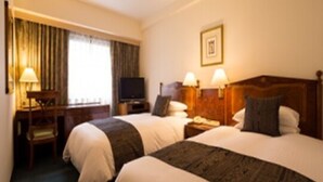A hotel room with two beds, a desk, a television, and a window with curtains.