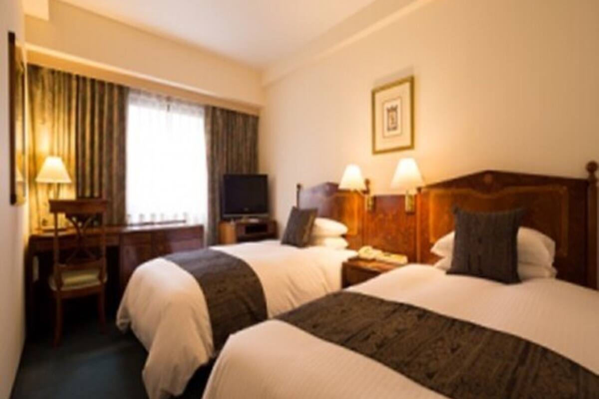A hotel room with two beds, a desk, a television, and a window with curtains.