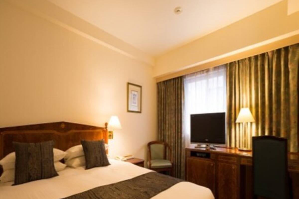 A hotel room with a large bed, a desk with a computer, a chair, and a TV.