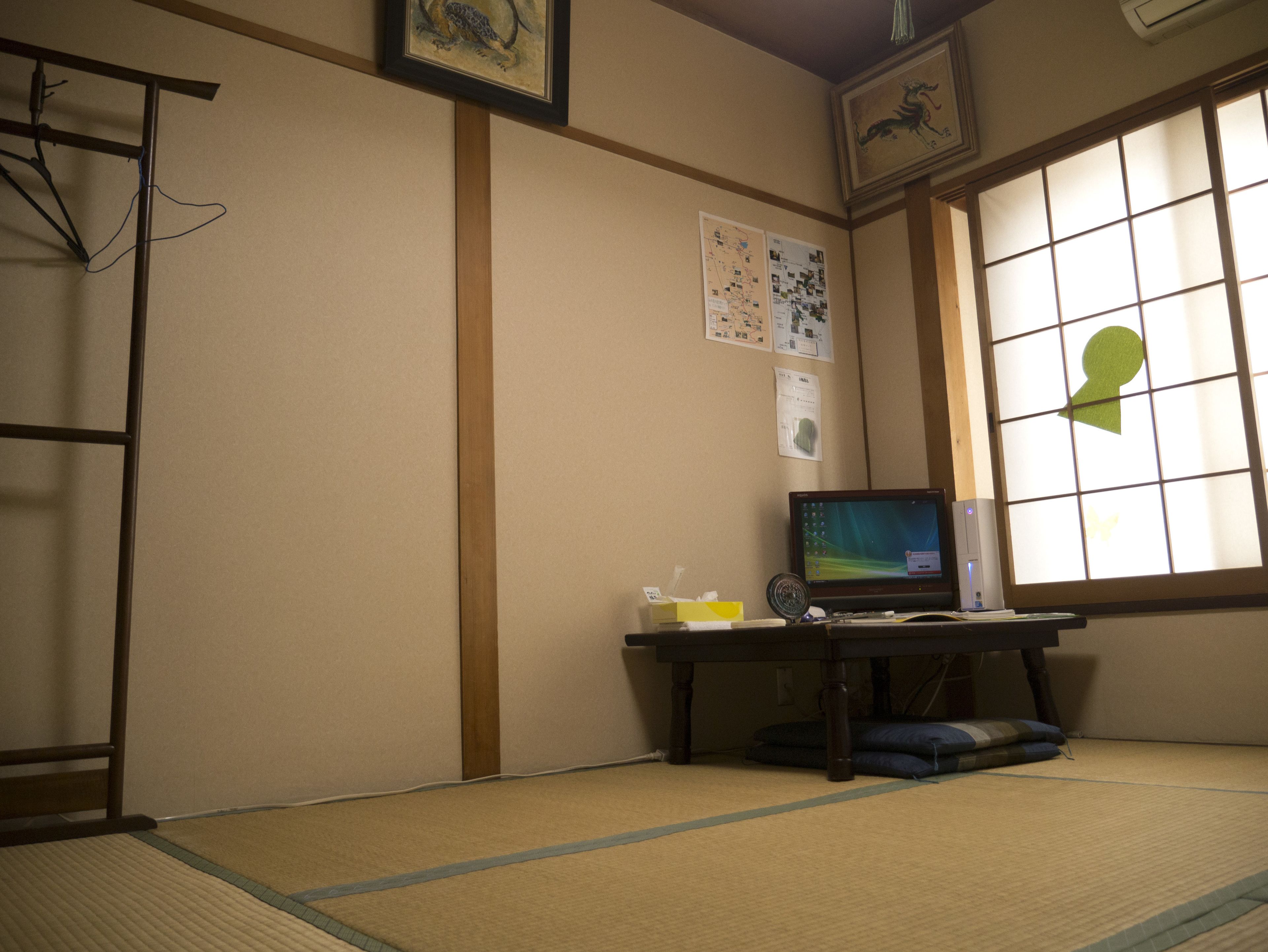 Una habitación japonesa tradicional con suelo de tatami, una mesa baja con una computadora y una ventana con celosías shoji.