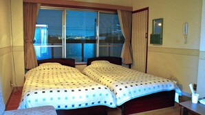 A hotel room with two beds, a window with curtains, a bedside table, and a view of the outside. - Yamabe Hotel (Tenri)