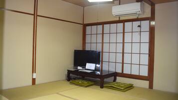 A traditional Japanese room with tatami flooring, a television on a wooden stand, and a sliding shoji screen.