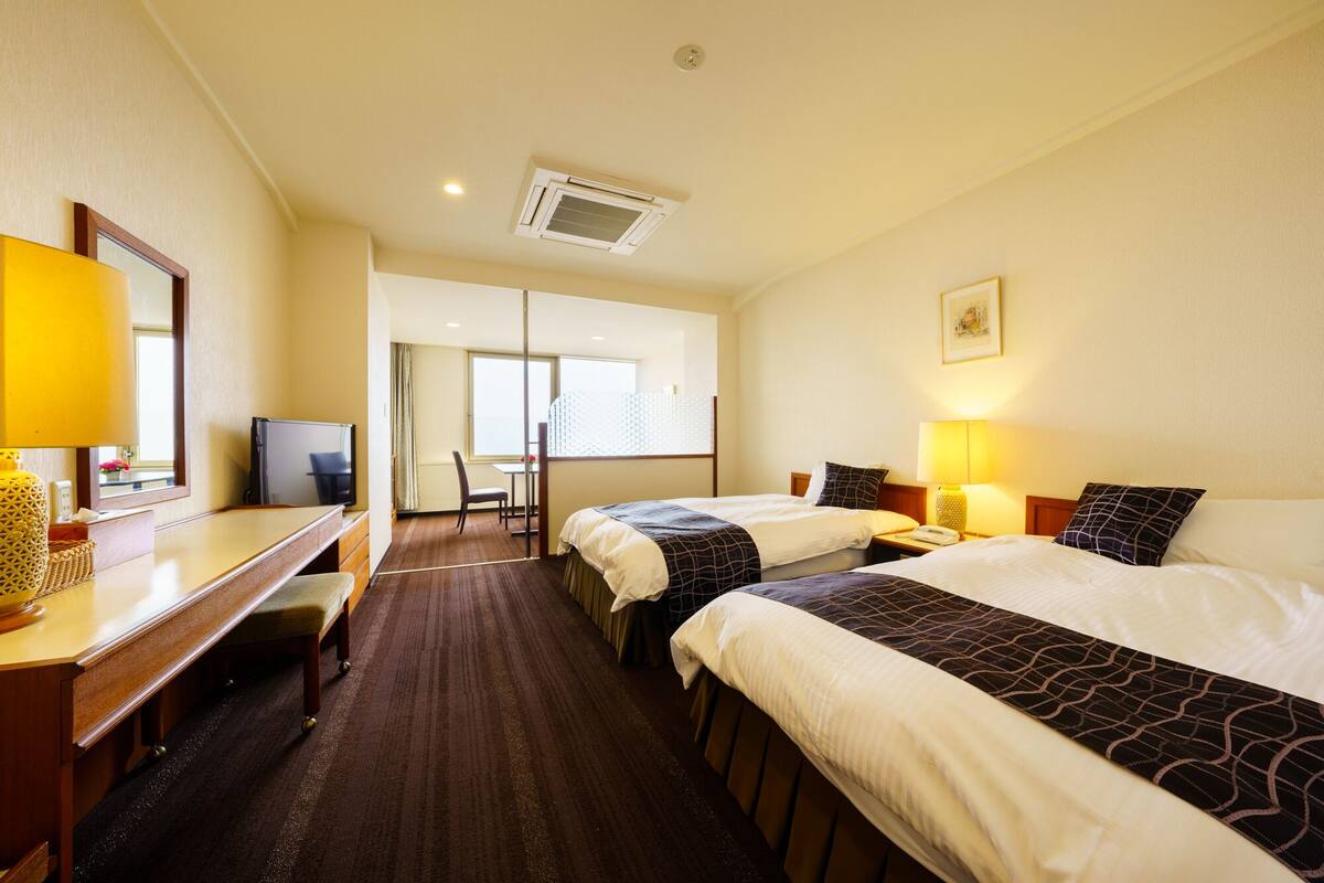 Una habitación de hotel con dos camas, un escritorio, una silla, un televisor y una ventana.