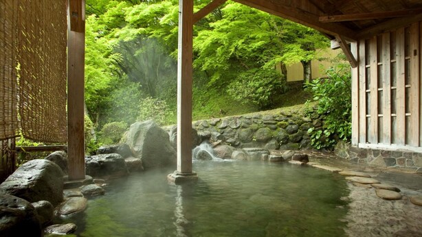 Un onsen japonais traditionnel, avec un bain en pierre, des piliers en bois et une clôture en bambou.