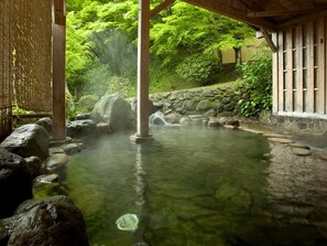 Un onsen japonés tradicional con una bañera de piedra, pilares de madera y una cerca de bambú.