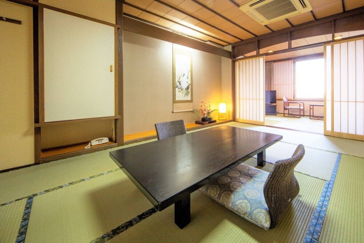 Una habitación japonesa tradicional con suelo de tatami, una mesa baja, una silla y puertas correderas.