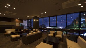 Un espace de détente moderne, doté de canapés, de fauteuils et de tables, et de grandes fenêtres offrant une vue sur la ville.